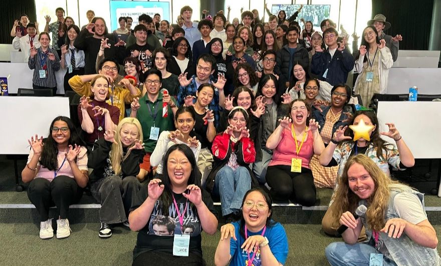 A group photo of the 2025 program in a lecture theatre making teeth with their fingers